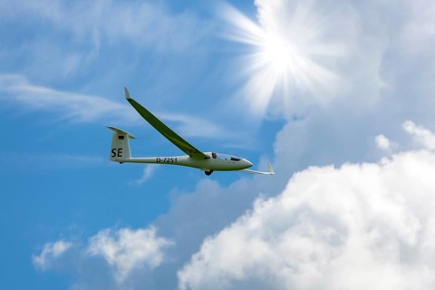 A glider flies through a blue sky with white clouds and bright sun, Baden-Württemberg, Germany