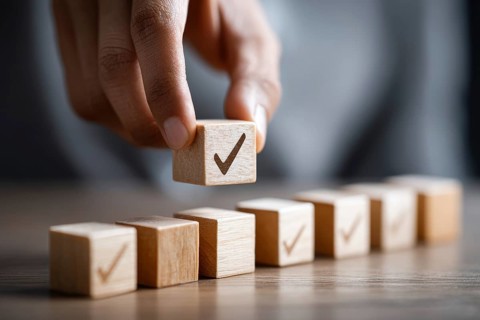 Checklist and task progress tracking concept. A hand placing the final checkmark on wooden blocks