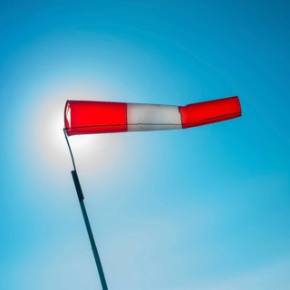 A vibrant windsock attached to a pole is fluttering in the wind against a clear blue sky. The