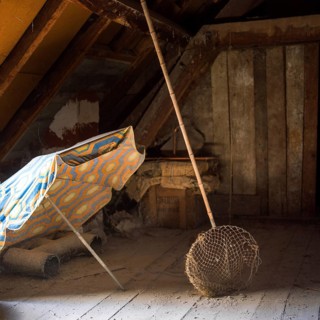 Sunlight filters through an attic, illuminating a colorful sunshade and a butterfly net alongside
