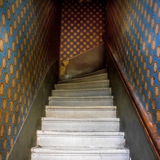 Staircase features worn steps and a dark atmosphere, going down to a lower level. The walls are