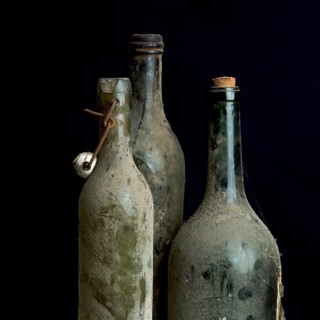 Three dusty vintage bottles stand together, covered in grime, highlighting their age and history.