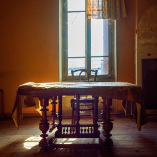 Warm sunlight filters through an old window, illuminating a vintage wooden table and chair. Dust