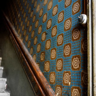 A close-up view of old wallpaper lining the walls of a staircase corridor, featuring a geometric