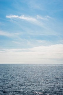 Dark ocean under a clear blue sky with bright white feathery clouds, cloud bank, horizon, water