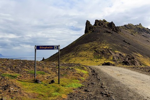 Gravel road with sign for place of interest, lava cave, Sönghellir lava tube, Stapafell mountain,