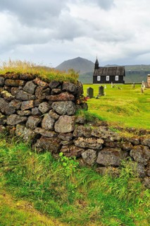 Traditional black church with cemetery, view through a stone wall to the wooden church Budakirkja,