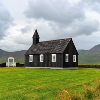 Traditional black church with white Tor tor in a meadow, wooden church Budakirkja, Búðir, Budir,