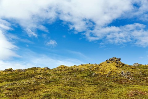 Volcanic rock, overgrown with moss, sparse vegetation, volcanic landscape, cumulus, text free