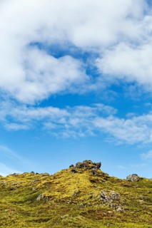 Volcanic rock, overgrown with moss, sparse vegetation, volcanic landscape, cumulus, text free