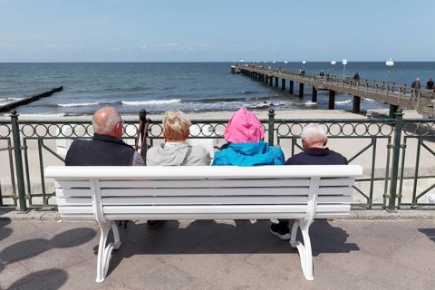 Holidaymakers sitting on a bench on the beach promenade, one is wearing strikingly colourful