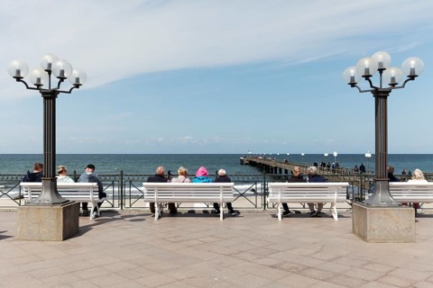 Holidaymakers sitting on benches on the beach promenade, one is wearing strikingly colourful