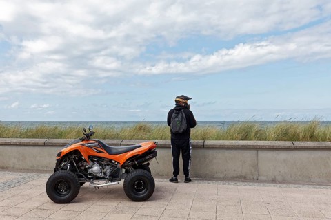 Motorcyclist with Kawasaki Quad Bike on the beach promenade, looking at the sea, Baltic resort