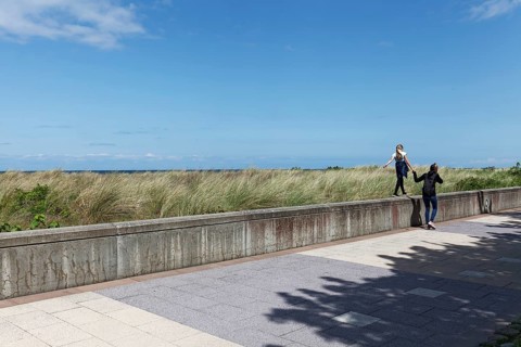 Teenager leads little girl by the hand over a wall on the beach promenade, Baltic resort