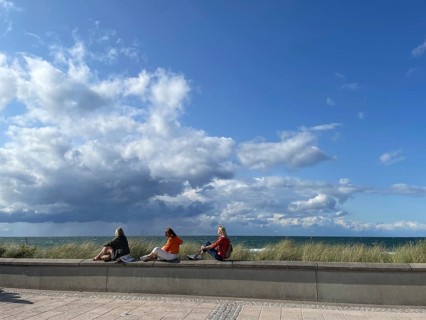 Three holidaymakers enjoying the sun, sitting on a little wall on the promenade, blue sky, Baltic