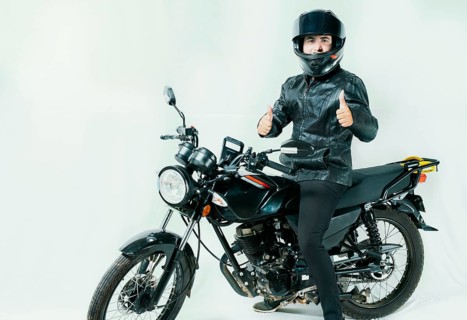 Smiling motorcyclist on his motorcycle with thumbs up, isolated. Motorcyclist with helmet on his