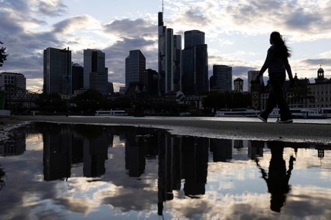 A woman walks along the banks of the Main in the rain in front of the Frankfurt banking skyline,