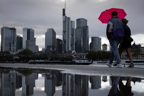 Two people walking in the rain under an umbrella in front of the Frankfurt bank skyline along the