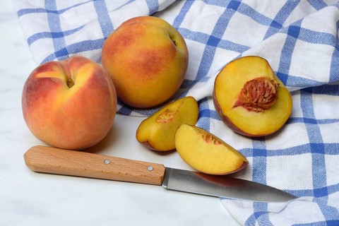 Peach with knife on kitchen towel, peach halves, Prunus persica