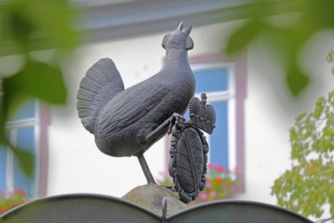 Grey bronze sculpture and coat of arms with crown at the Hennebrunnen fountain, bird figure,