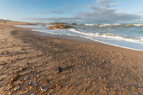 The waves crash gently against a rocky shoreline at sunset, creating a tranquil atmosphere. The