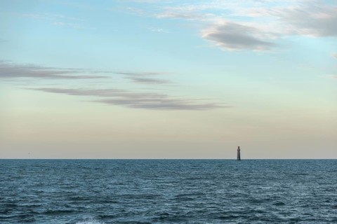 A lighthouse rises from the gentle waves of the ocean, surrounded by a tranquil seascape. Soft