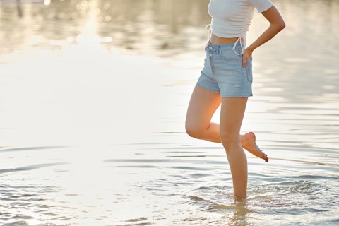 Unrecognizable woman steps carefully in the clear water, enjoying the warmth of the sun on her skin