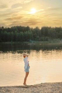 A woman stands at the edge of a tranquil lake during sunset, gazing across the water. Warm golden