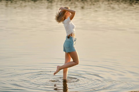 A young woman is joyfully splashing in the shallow waters of a serene lake. The sun is setting,
