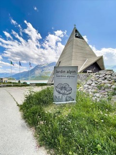 In front sign for Jardin Alpin, behind it pyramid museum with stylised pyramid in memory of the
