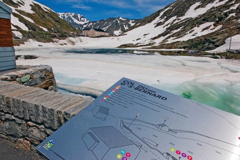 Tourist information board of Great St. Bernard Pass, behind it pass summit with icy lake Lago di