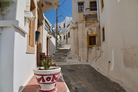 Narrow alley with white buildings and flower pot, old plaster, quiet and sunny atmosphere, Agia