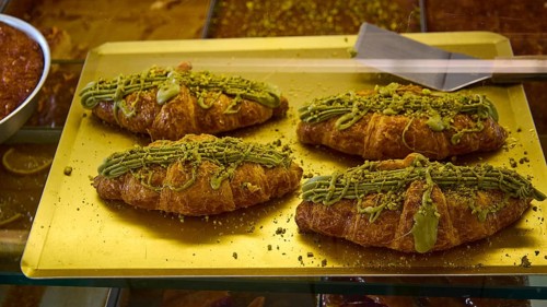Four croissants decorated with pistachio cream on a golden tray, appetising and fresh, Agia Marina,