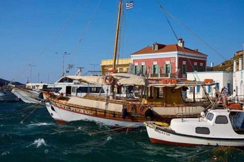 Wooden boats in the harbour with bright facades and Greek flags in calm waters, Agia Marina, Leros,