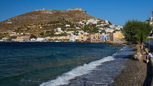 Panteli fortress, beach with pebbles, wavy sea, coast with colourful buildings and hills in the