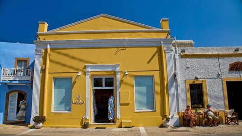 Yellow building with neoclassical facade, people in front of the door, clear blue sky, traditional