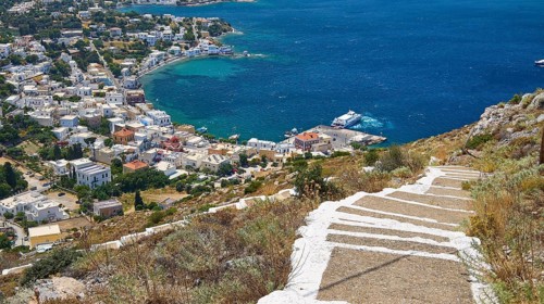 Ormos Alintas, stone path leads to a coastal village with bright blue sea and deep blue sky, Agia