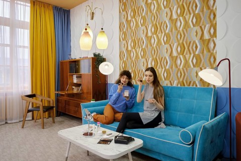 Two friends are seated on a vibrant blue sofa in a stylish living room filled with natural light