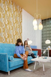 Two friends enjoy a cozy moment in a modern lounge, sitting on a colorful sofa. One woman removes