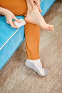 Unrecognizable woman use electric gadget to peel her heel from rough or dead skin while sitting on