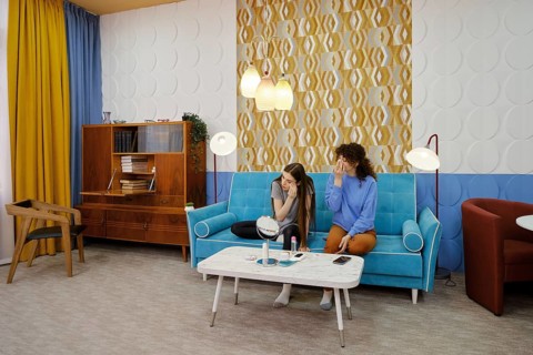 Two women sit on a turquoise sofa in a stylish living room and removing makeup. The vibrant decor