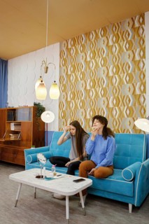 Two women remove makeup from their faces sitting at home on a blue couch in a cozy living room,