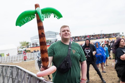 A festival visitor stands with an inflatable palm tree in the rain at the Highfield Festival on