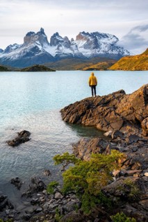 Young man on the shore of the blue lake Lago Pehoe in the evening light, Cuernos del Paine mountain
