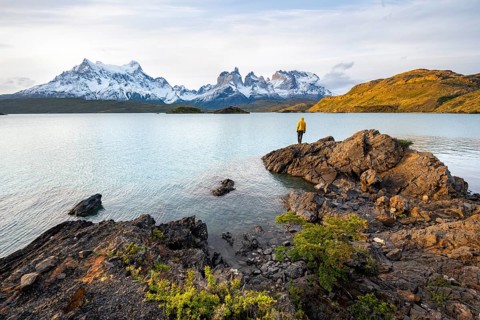 Young man on the shore of the blue lake Lago Pehoe in the evening light, Cuernos del Paine mountain