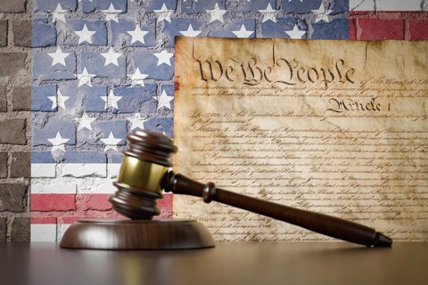 United states constitution and american flag on wall with gavel resting on table in front