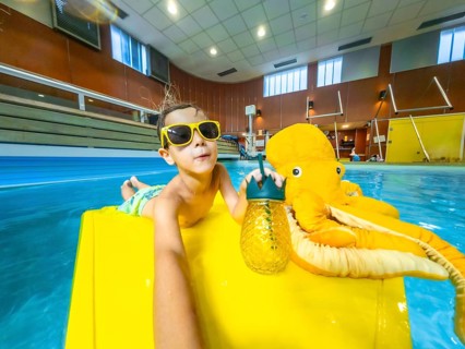 Young boy enjoys summer vacation, relaxing on a yellow float with a plush octopus and a refreshing
