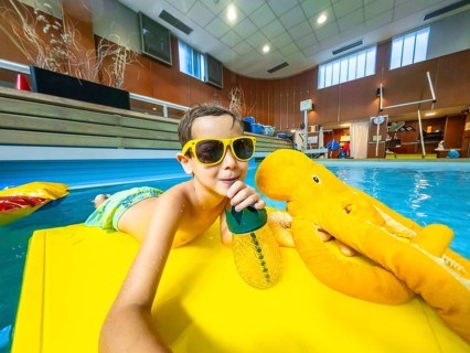 Young boy wearing sunglasses enjoying a refreshing drink while floating on a yellow raft with a