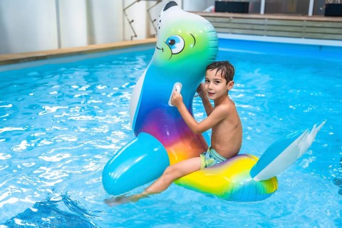 Boy enjoying summer holidays while riding an inflatable toy in a vibrant blue swimming pool,