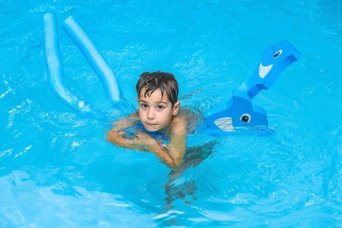 Boy swimming and playing with pool noodles and inflatable toy in a blue swimming pool during summer